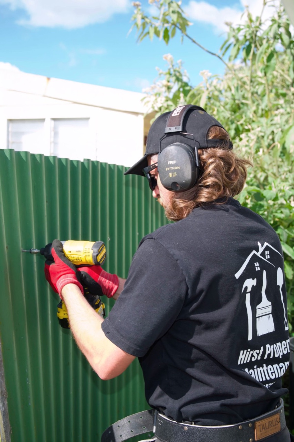 Property maintenance worker drilling a green corrugated fence