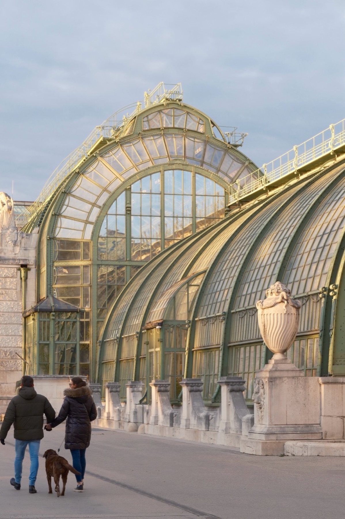 Couple walking a dog beside a historic glasshouse