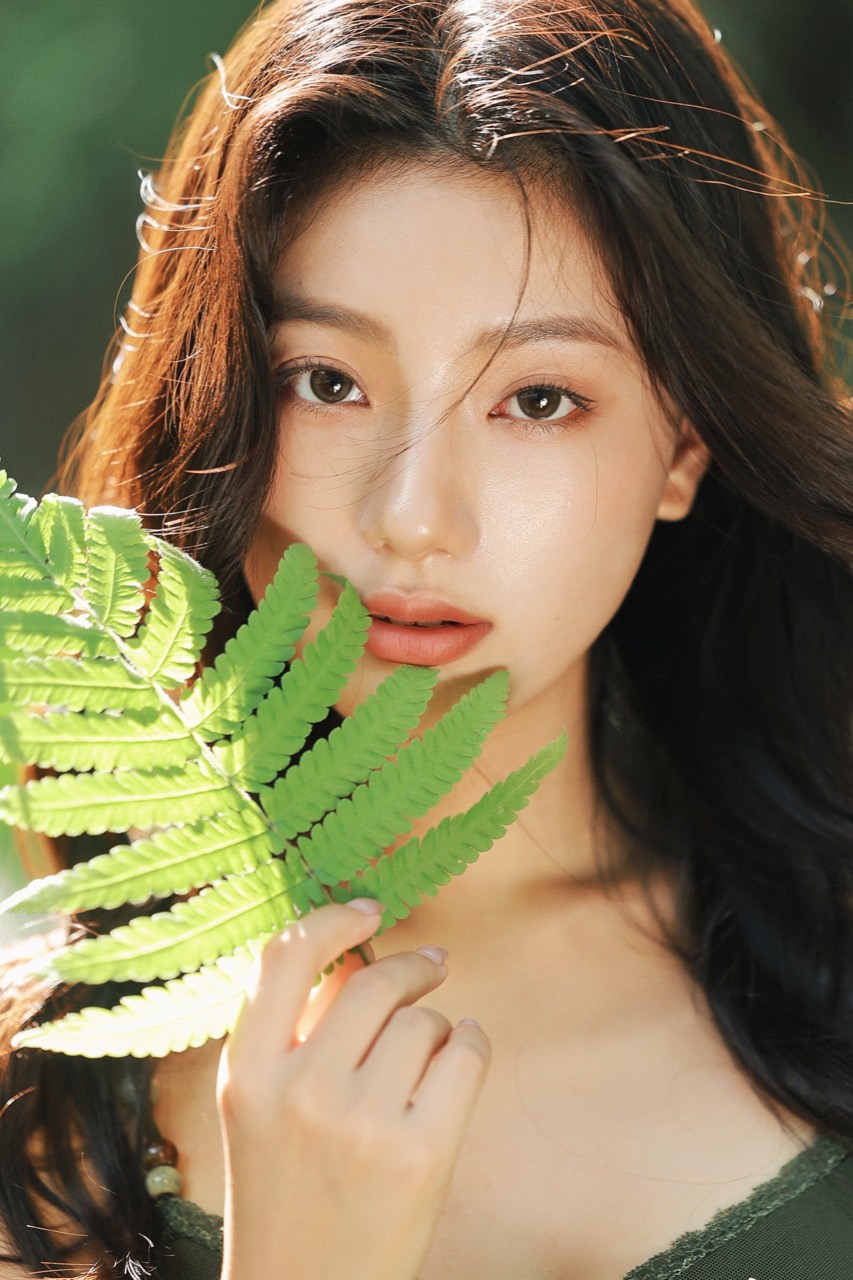 Close portrait of a woman holding a fern in warm forest light