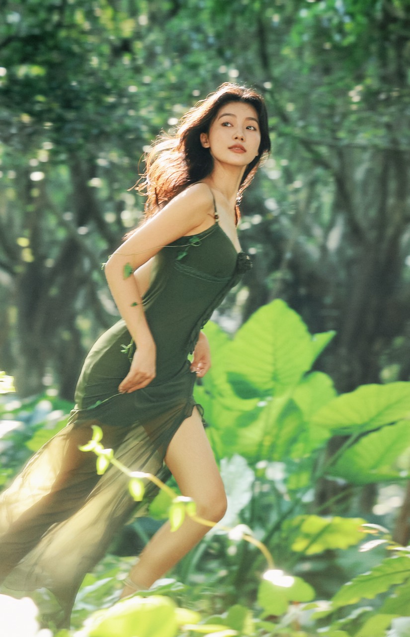 Woman in a flowing green dress moving through a sunlit forest