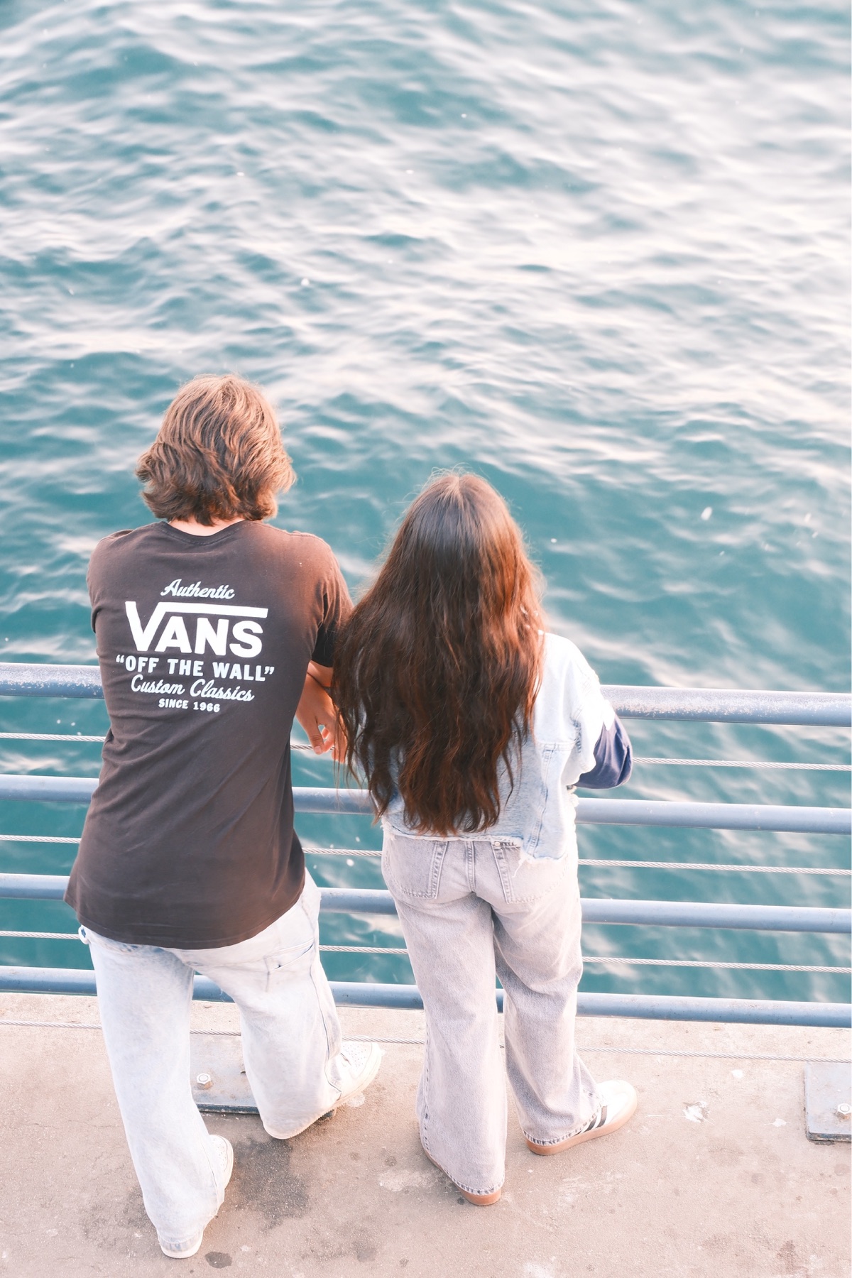 Two people seen from behind looking across blue water